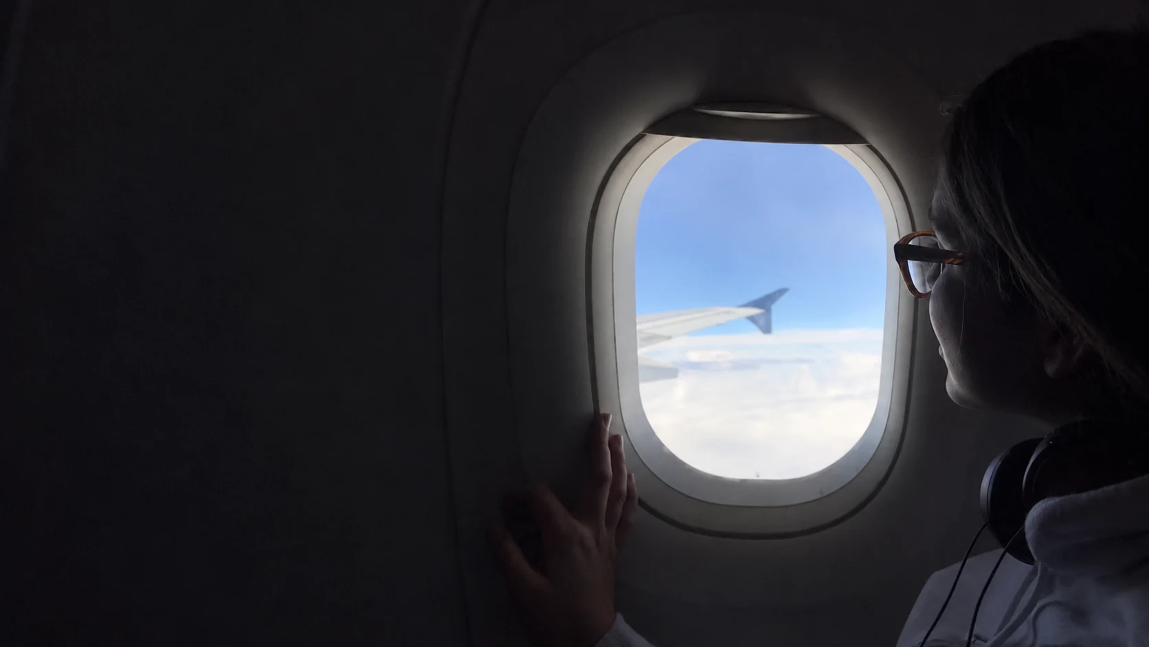 Una pasajera con audífonos mira el cielo y el ala del avión por la ventanilla.